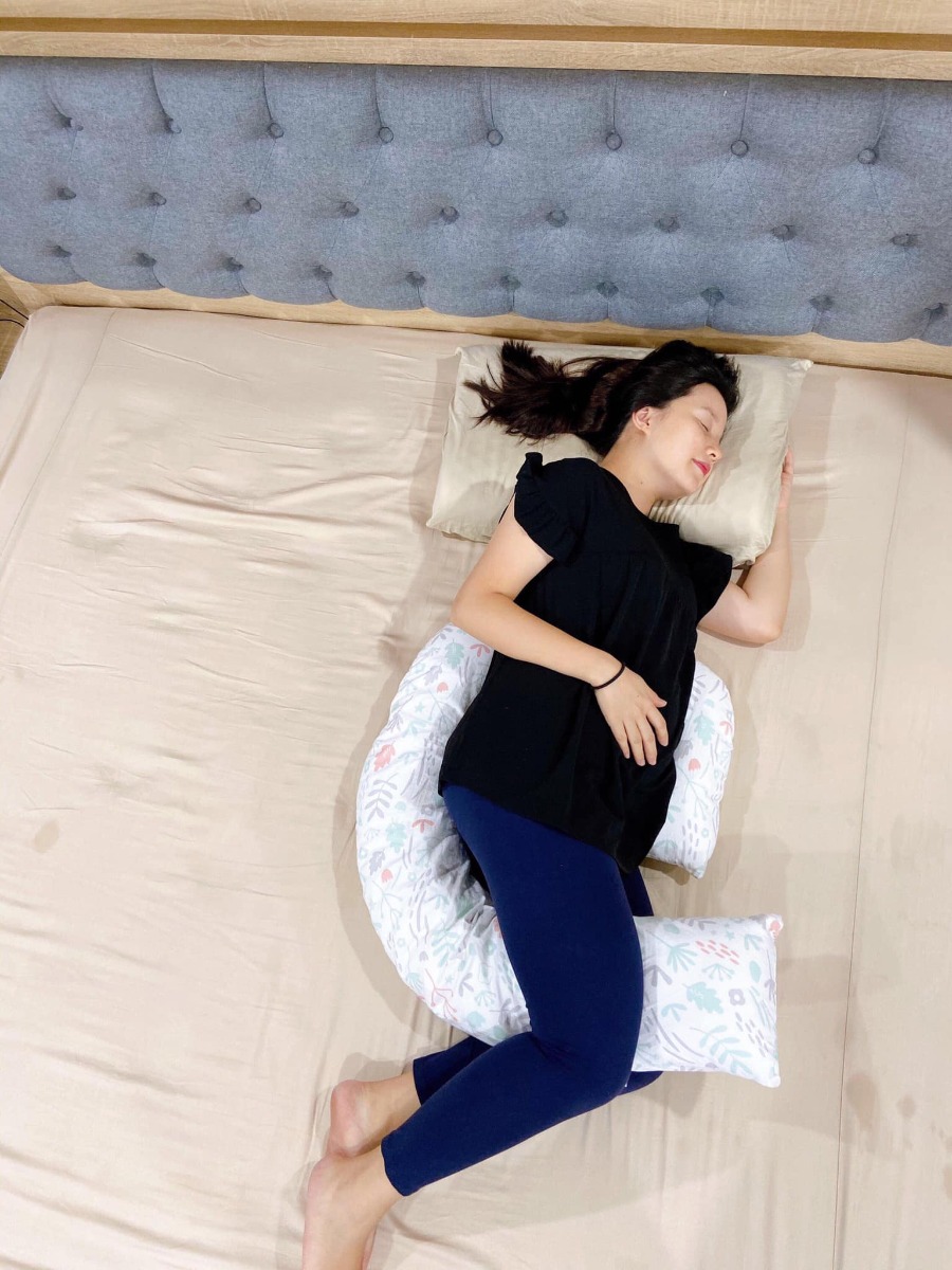 Đẻ đến bạn thứ 4 rồi mà mãi đến lần chót chốt sổ này mới phát hiện ra bao nhiêu thứ hay ho dành cho mẹ bầu lẫn cho con bú, có những món đồ dùng vừa đa năng, vừa hiệu quả mà mình ước gì có thể biết sớm hơn!

Hôm trước mình chia sẻ cái cốc hứng sữa kiêm hút sữa, chắc nhiều bạn sau đó đã được “kiểm nghiệm” độ vi diệu rồi đúng ko? Hôm nay mình “khoe” thêm cái gối này!

Đây là chiếc gối bầu đa năng DREAMGENII, được “khai sinh” ở Anh, và sản xuất tại Thổ Nhĩ Kỳ. Nhìn thì đơn giản thế thôi, nhưng có sử dụng mới thấy từ thiết kế tới chất liệu, đường may… đều cực kỳ lợi hại, và nó hoàn toàn có lí do để có giá bán cao gấp 6-7 lần các loại gối bầu đang bán phổ biến hiện giờ.

- Khi bầu thì dùng để điều chỉnh tư thế ngủ, nâng đỡ toàn bộ cơ thể, giúp mẹ bầu có tư thế ngủ đúng, giấc ngủ ngon và sâu hơn. Đặc biệt là những tháng cuối thai kỳ, bụng to, chèn ép nhiều, mình không thể nằm ngủ nổi mà không có cái gối này luôn!

- Tùy từng vị trí nâng đỡ cơ thể của mình mà gối có độ mềm khác nhau chứ không nhồi bự bông, dày sụ và cứng ngắc như loại gối bầu chữ U mình từng dùng qua. Gối DREAMGENII này vừa nhẹ vừa mềm, gọn gàng nữa chứ không nặng chịch hay cồng kềnh. Chính vì thiết kế về hình dạng và chất liệu bông nhồi (100% bông Thổ Nhĩ Kỳ) nên khi hỗ trợ mẹ bầu rất tốt, giảm đau nhức, chuột rút và đau vùng xương chậu.

- Tới giai đoạn sau sinh, gối này cũng thay thế luôn gối chữ C, giúp nâng đỡ phần hông của mẹ và toàn bộ cơ thể của em bé khi mẹ ngồi cho con bú. Mình cũng từng dùng qua gối chữ C rồi, và với mình thì cái gối DREAMGENII này còn lợi hại hơn gối chữ C vì có thêm phần nâng đỡ đầu của bé, giúp mẹ có thể rảnh tay, không cần tới 1 tay đỡ phần đầu của con mà đầu vẫn luôn ở vị trí cao hơn dạ dày, đảm bảo tu ti thoải mái và không lo bị sặc sữa/nôn trớ! Mình lại chủ yếu là ngồi cho bú để con bú xong là mẹ cũng ngồi luôn đó vỗ ợ cho con luôn, nên lại càng thấy cái gối này siêu tiện!

- Vỏ gối được làm bằng chất liệu cotton tự nhiên 100%, rất mịn và thoáng, mình đã trải qua cả mùa hè ôm bụng bầu nằm ngủ với cái gối này và luôn có cảm giác mát mẻ khi ôm gối. Vỏ cũng dễ dàng tháo ra để giặt nhé.

- Gối bầu DREAMGENII cũng là sản phẩm được Bộ Y tế của Anh cấp chứng nhận là dụng cụ y khoa, và được sử dụng trong bệnh viện phụ sản ở Anh đấy!